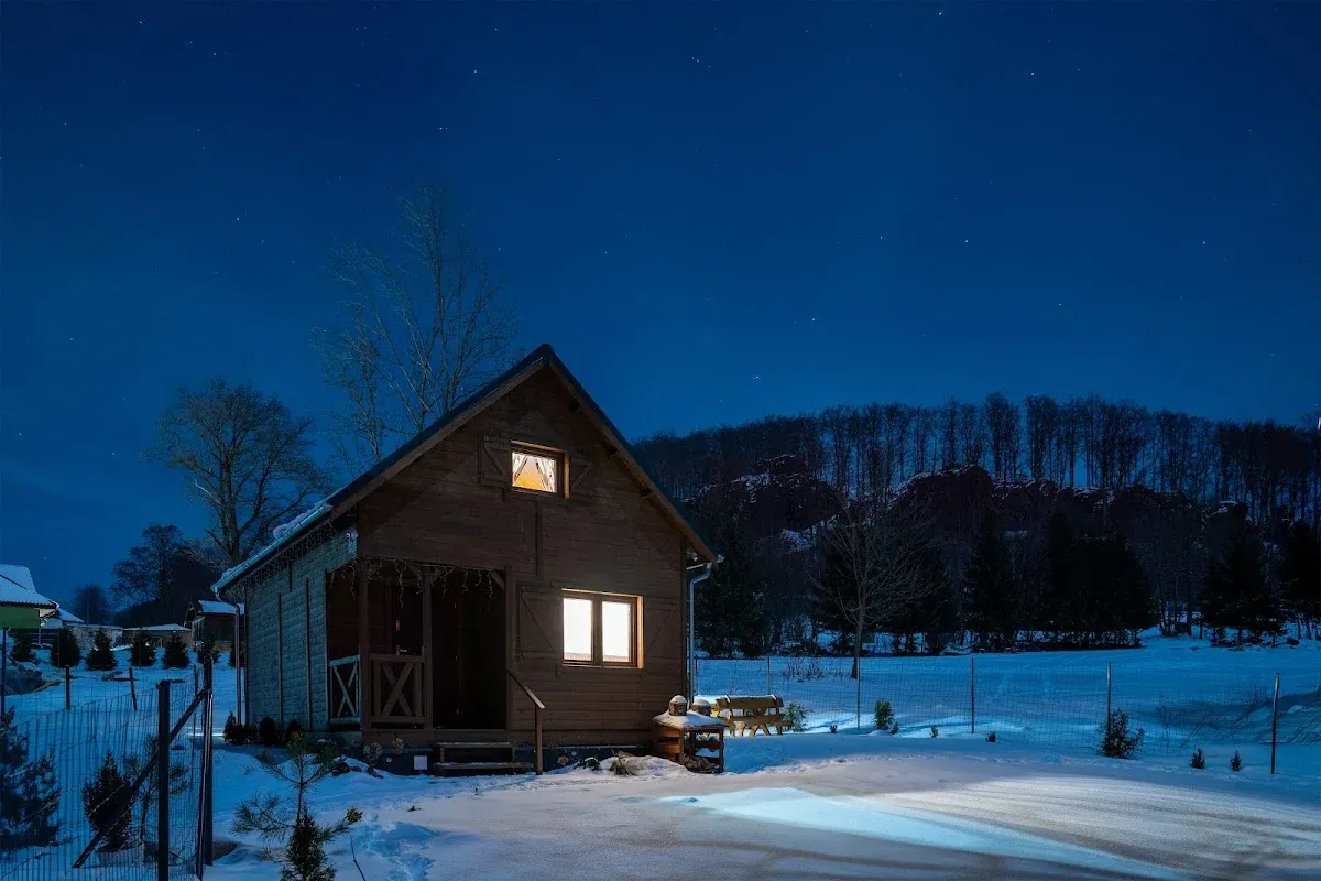Nocny widok na oświetlony domek na tle górskiej panoramy.