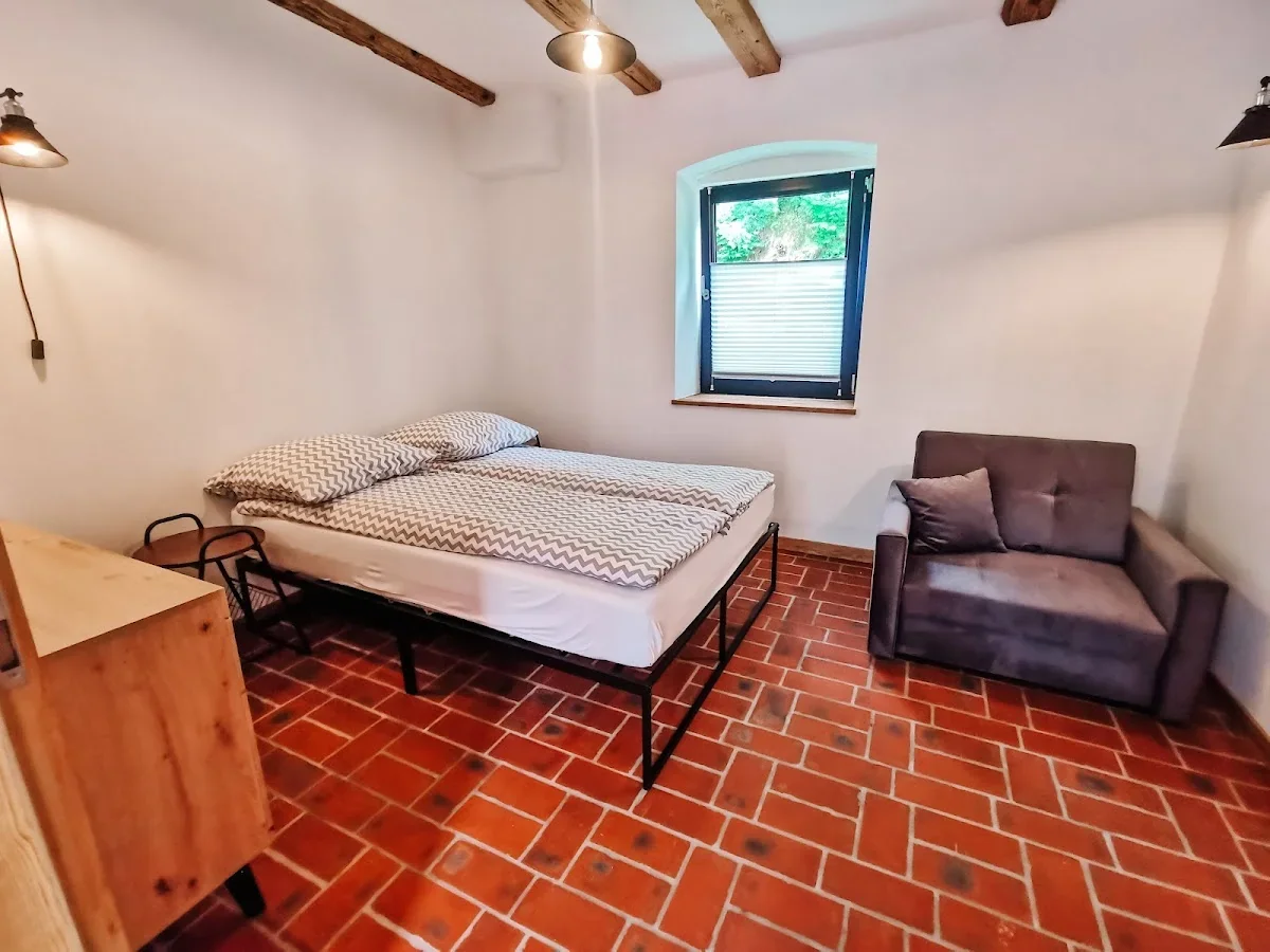 Pokój o białej tonacji z łóżkiem małżeńskim o jasnej pościeli.